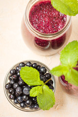 Blueberry smoothie decorated with fresh green mint leaves and raw ripe berries on yellow pastel background.