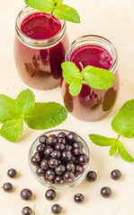 Currant smoothie decorated with fresh green mint leaves and raw ripe berries on yellow pastel background.