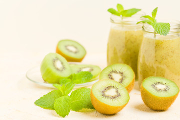 Kiwi smoothie decorated with fresh green mint leaves and raw ripe cut fruit on yellow pastel background.