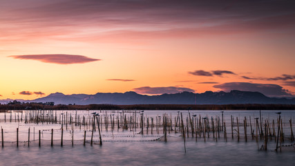 Fototapeta na wymiar Amanece naranja en lago con montañas en el horizonte
