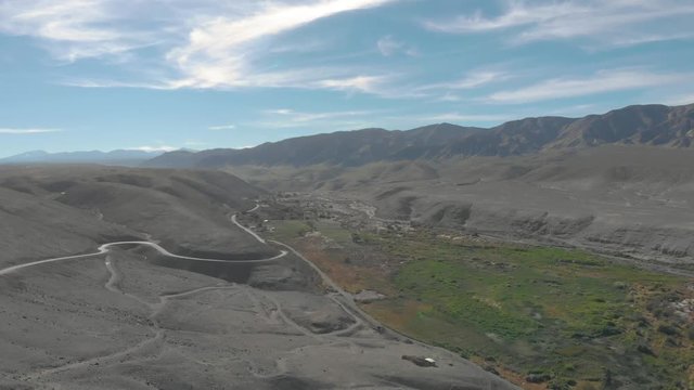 Aerial cinematic view of green valley in Atacama desert Tarapaca Chile. Drone rising up filming trees, plants and river between vast dry rocky and sand desert. Mountain at horizon in landscape. 