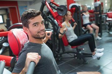young adult doing powerlifting on machines in fitness club
