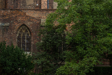 old arch window on brown brick wall of ancient church background texture behind green trees 