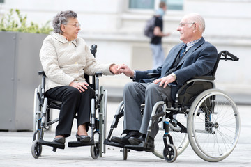 Fototapeta na wymiar old couple in wheel chair holding hands