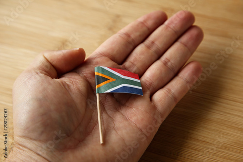 A Caucasian hand holding a small South African flag.