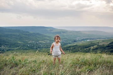Fototapeta na wymiar boy in a beige light overalls walking on the field in the mountains in the summer evening alone