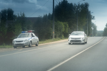 Obraz na płótnie Canvas Police car on the roadside. Rural asphalt road with a white car
