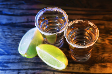 Two glasses of tequila and slices of lime on a wooden background