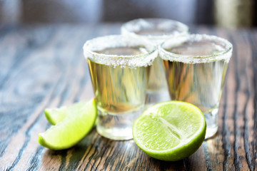 Three glasses of tequila and limes in a defocus on a blurred background