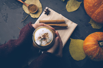Pumpkin spice latte or coffee with cinnamon. Autumn, fall or winter hot drink. Background with yellow leaves