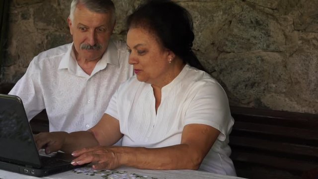 adult senior couple with laptop at courtyard. women is showing something interesting to man. man with astonish amaze daze expression on face