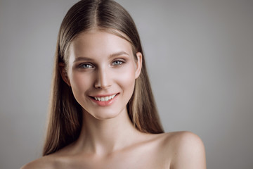 Portrait of a beautiful young girl with nude make-up in studio on a gray background