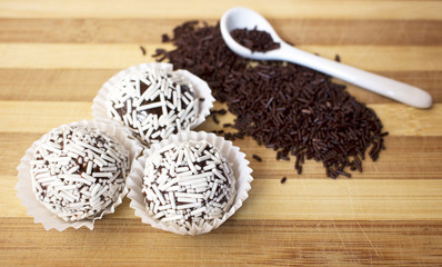 Brazilian brigadeiro delicacy with white sprinkles in wooden table, with white spoon on top of chocolate sprinkles.