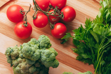 On a dark wooden table, on a round wooden board fresh green broccoli, parsley, dill and cherry tomatoes for your health. Recipe. Ingredients. Dietary food. Place under the text. View from above