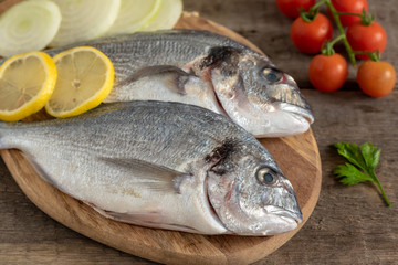 Fresh dorada fish with vegetables on wooden background.