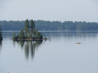 View of Damariscotta Lake in Maine with a person on a kayak passing an island 