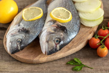 Fresh dorada fish with vegetables on wooden background.