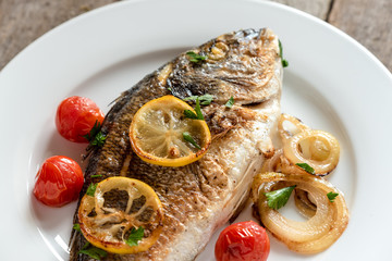 Dorada on plate with onions, lemon and cherry tomatoes
