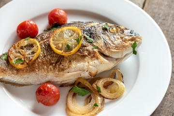Dorada on plate with onions, lemon and cherry tomatoes