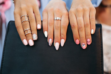 Crop of girls showing her stylish manicure, holding thair fingers on black leather handbag....