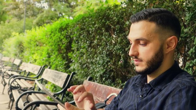 Young Arabian European searching in tinder on a Tablet in the Park