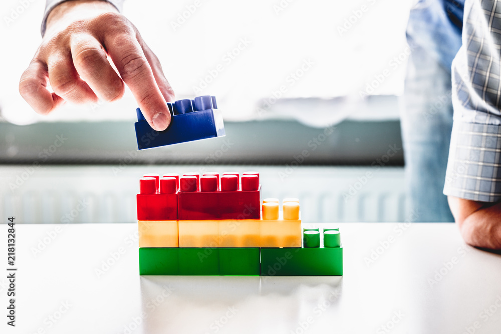 Poster the businessman arranges blocks of different colors. the man arranges the blocks to form stairs. gro