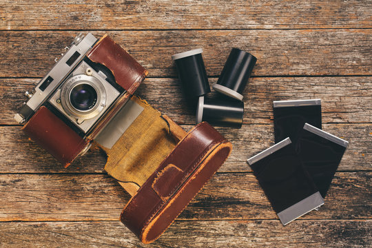 Vintage 35mm film camera in worn leather case with film canisters and prints on weathered wooden background