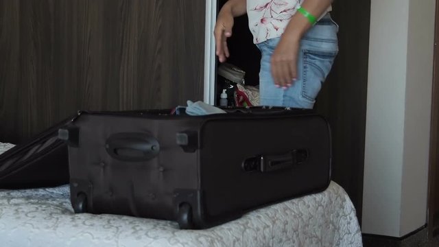Woman with a suitcase. A woman in a hotel room puts things in a suitcase.