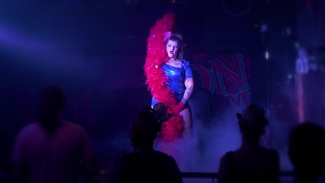 Wide shot of a curvy burlesque dancer doing a suggestive sexy dance on stage with a red feather boa