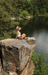 Fototapeta na wymiar Young woman on rocky mountain near lake. Camping season
