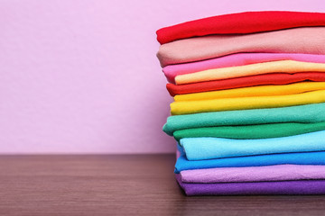 Stack of colorful t-shirts on table against color background