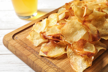 Wooden board with crispy potato chips on table, closeup
