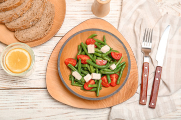 Plate with tasty green beans, tomatoes and cheese on wooden table, top view