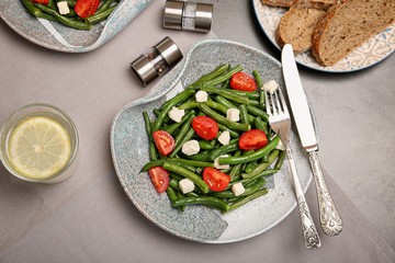Plate with tasty green beans, tomatoes and cheese on table, top view