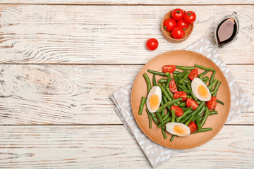 Plate with tasty green beans, eggs and  tomatoes on wooden table, top view