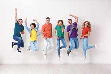 Group of young people in jeans and colorful t-shirts jumping near light wall