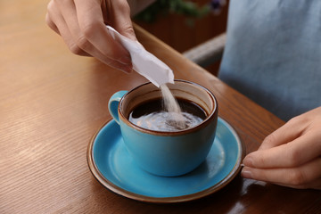 Woman adding sugar to fresh aromatic coffee at table, closeup