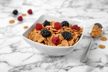 Bowl with cornflakes and berries on marble table. Whole grain cereal for breakfast
