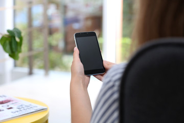 Woman holding smartphone with blank screen on blurred background. Mockup for design