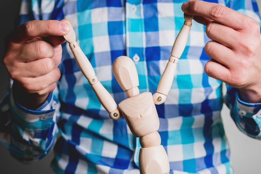 The man is holding a wooden mannequin. Control and control of the manikin, other people. Business concept, coaching and human manipulation. Controlling other people.