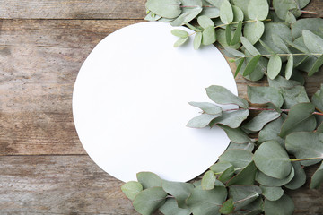 Fresh eucalyptus leaves and blank card with space for design on wooden background, top view