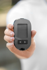 Woman holding digital glucometer on blurred background. Diabetes control