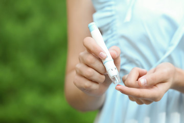 Woman using lancet pen on blurred background. Diabetes control
