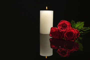 Beautiful red roses and candle on black background. Funeral symbol