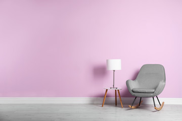 Rocking chair and lamp on table near color wall with space for text. Interior element