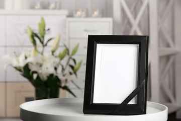 Funeral photo frame with black ribbon on table, indoors