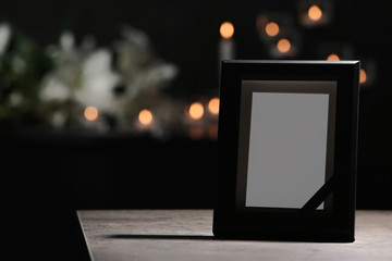 Funeral photo frame with black ribbon on table in dark room