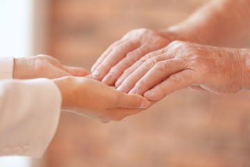 Young woman holding elderly man hands indoors, closeup. Help service