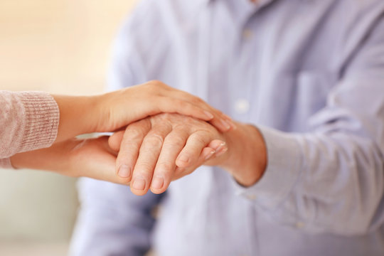 Young woman holding elderly man hand, closeup. Help service