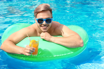 Young man with cocktail in pool on sunny day